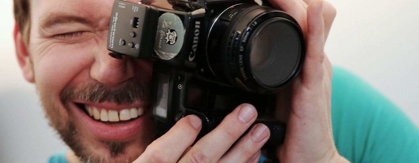 Portraitfoto von Christoph Uiberacker mit Fotoapparat vor Gesicht