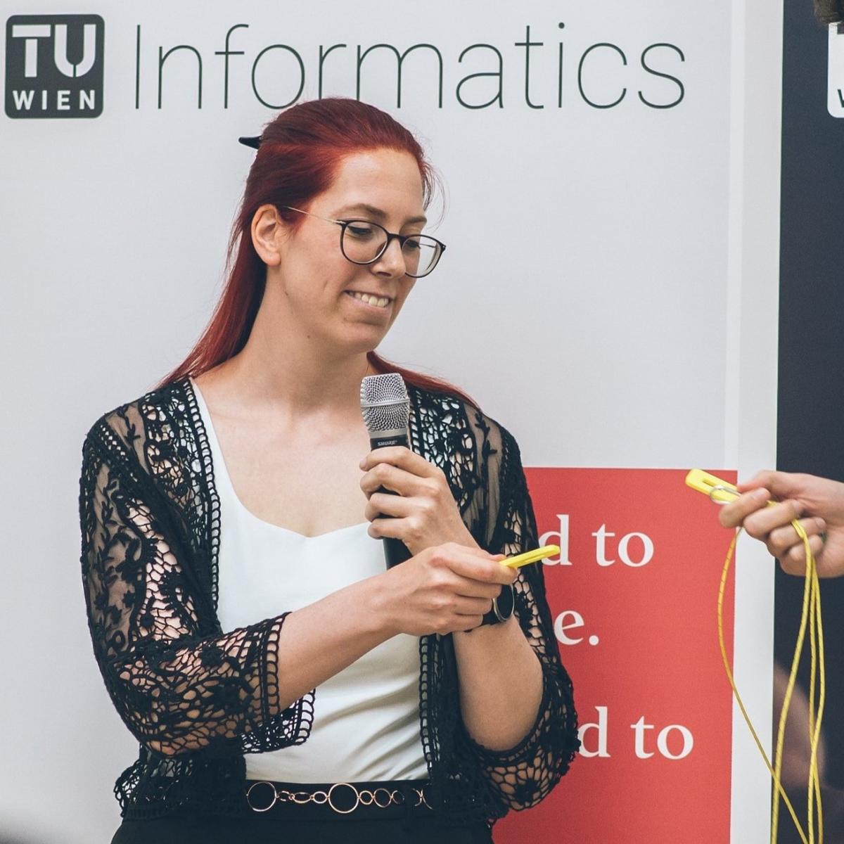 Martina Landman mit einem Mikrofon in der Hand und einem 3D-Druck Element beim Vorführen einer CS Unplugged Aufgabe